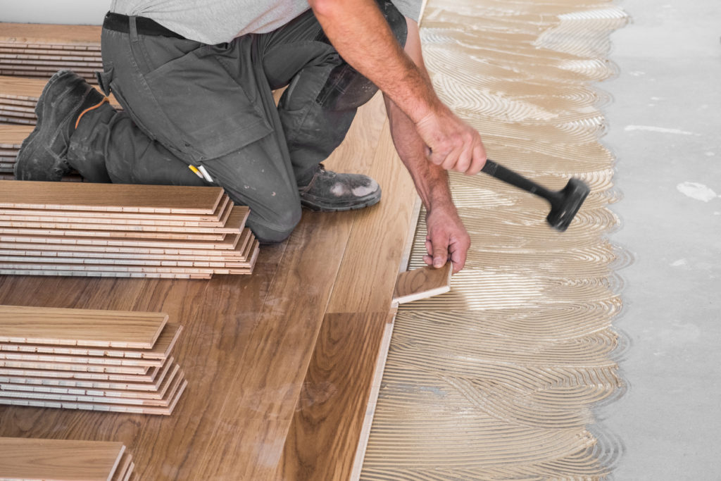 Worker installing wooden flooring boards on applied adhesive